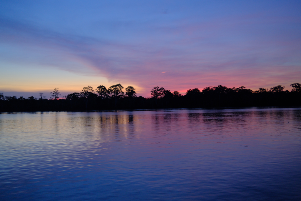 Sunset over the Peruvian Amazon River with pink and purple skies reflecting on calm waters during a Delfín Amazon Cruises expedition