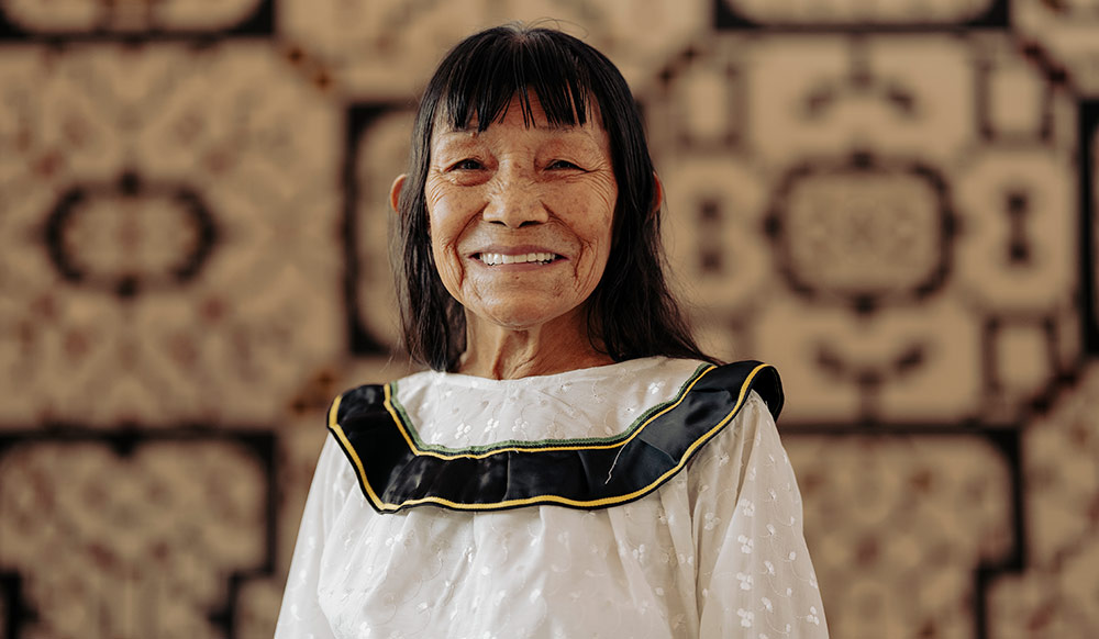 Sara Flores in traditional Shipibo dress with kené tapestries behind her