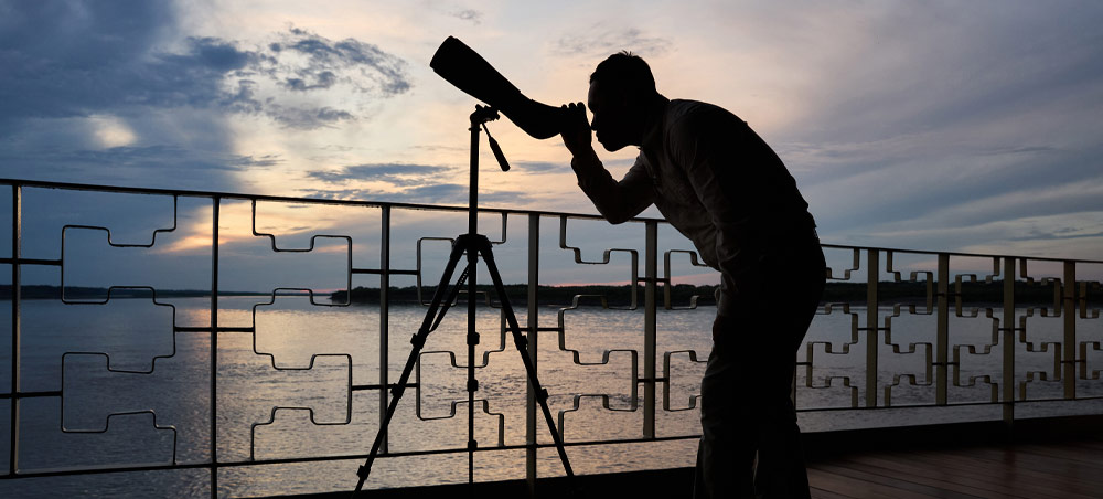 Guest using a telescope at dusk aboard a Delfín Amazon cruise