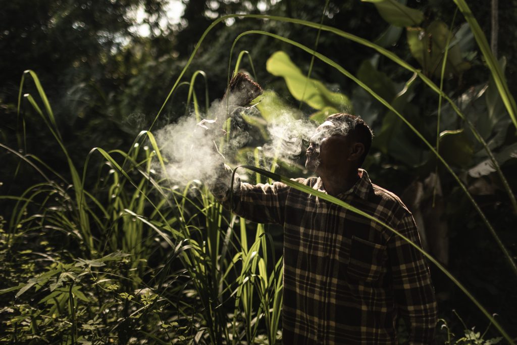 Man holding smoking plant material amid vegetation in the Peruvian Amazon