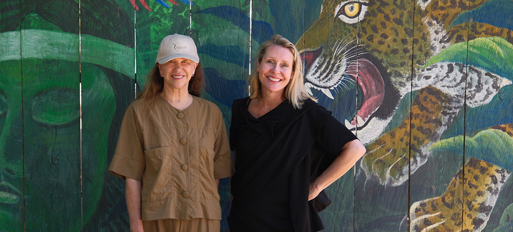 Two women standing in front of a rainforest wildlife mural
