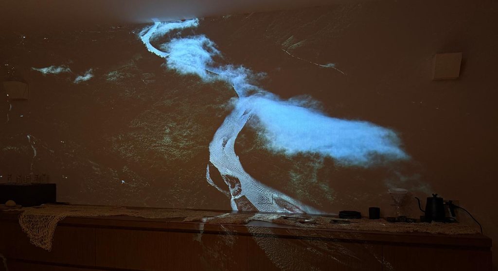 A river landscape projected onto the wall above a tasting table in a darkened room.